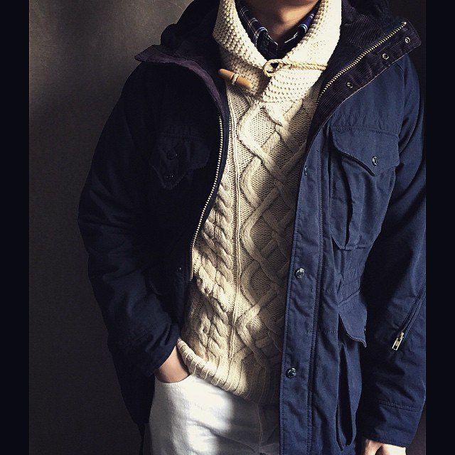 Une parka Engineered Garment, portée par dessus un pull Ralph Lauren et une chemise en flannelle