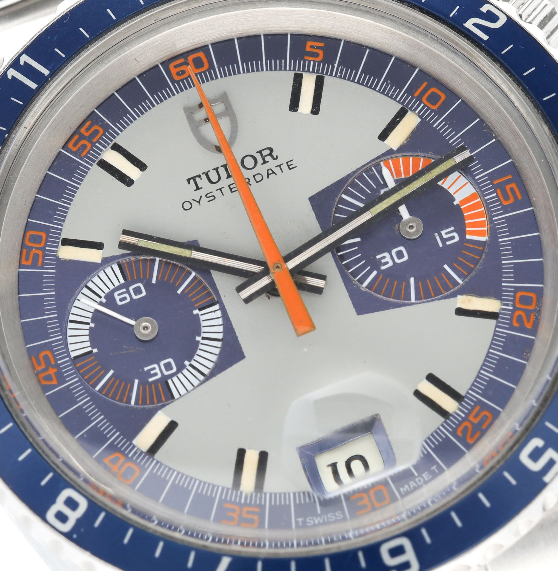 Primer plano de la esfera de un cronógrafo Tudor 7169/0 Monte Carlo: fondo gris, contadores azules, trotadora naranja, fecha a las 6h con lupa. La densidad visual recuerda a un casino.