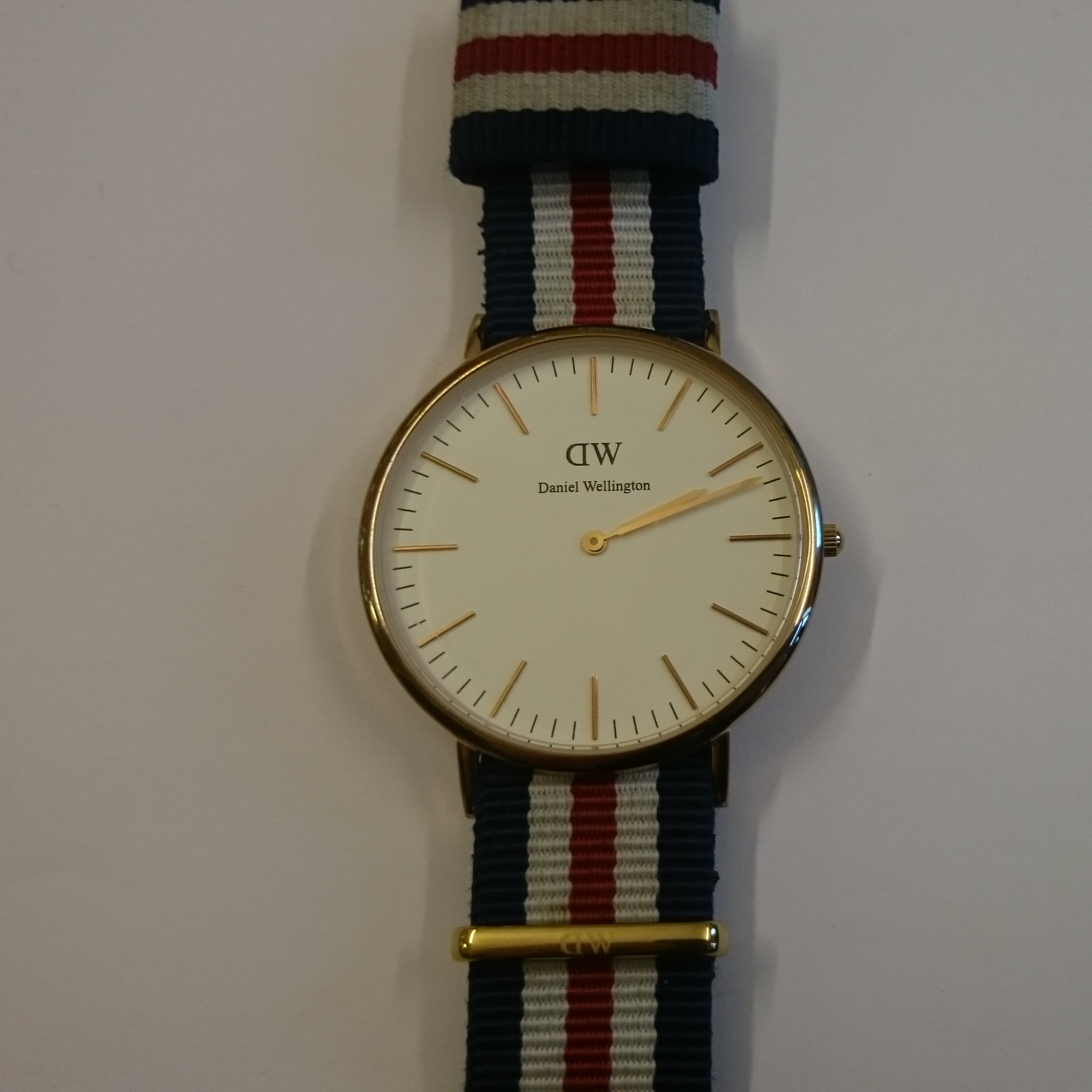 Montre Daniel Wellington Classic, cadran blanc minimaliste, boîtier or rose 40mm, bracelet NATO tricolore.